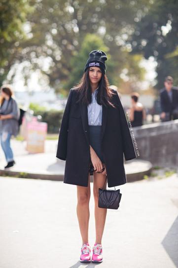 Девушка в короткой юбке, кроссовках и черном пальто