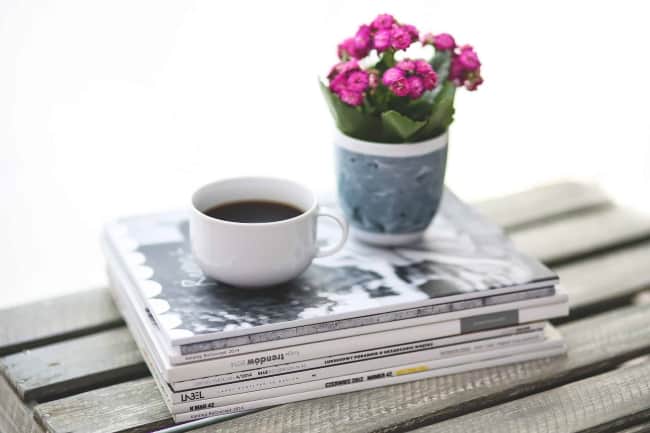 stack of magazines with coffee mug and flowers on top